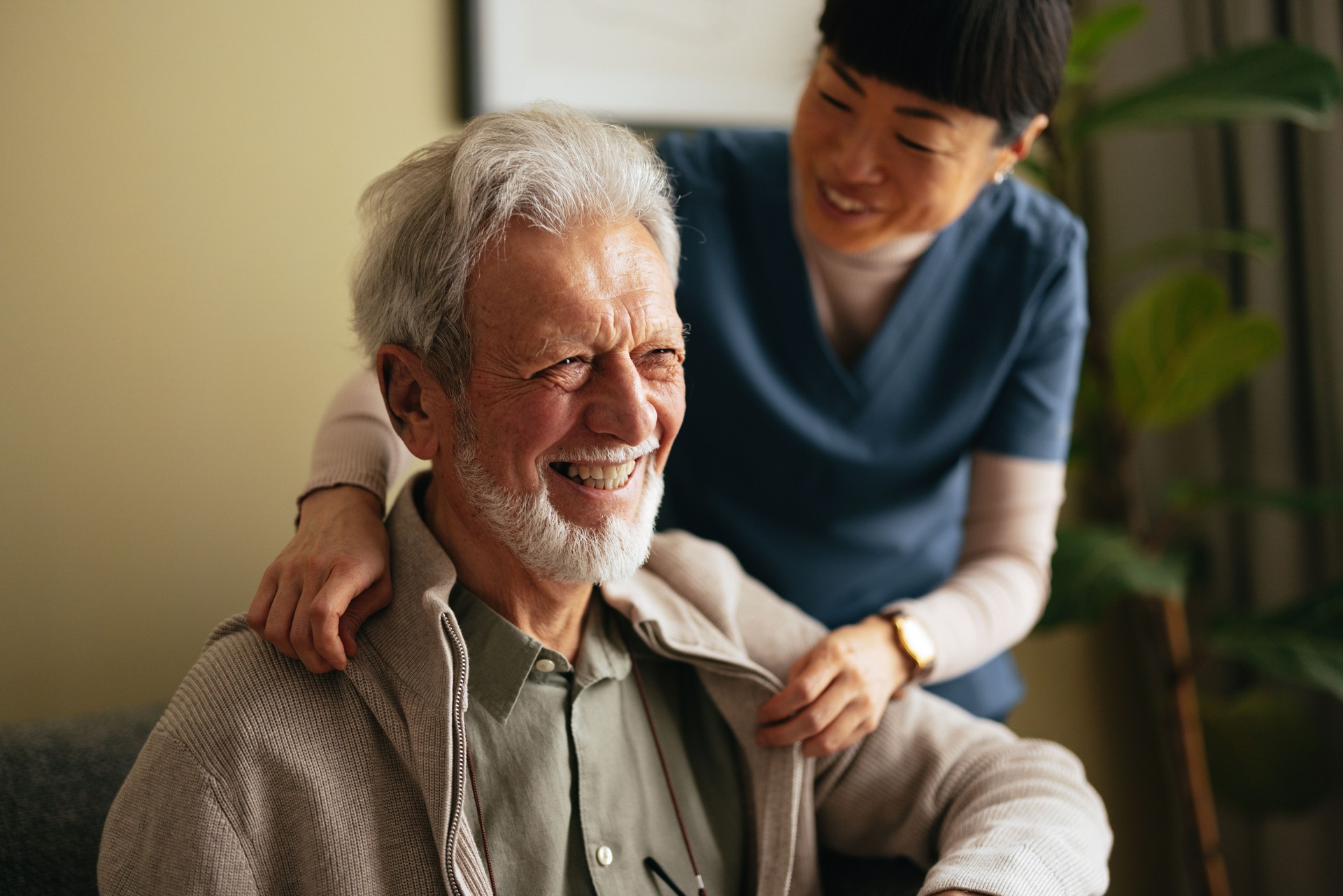 Portrait of a Smiling Elderly Man Taking a Jacket off With a Help of a Woman in a Huntersville, North Carolina Care Home.