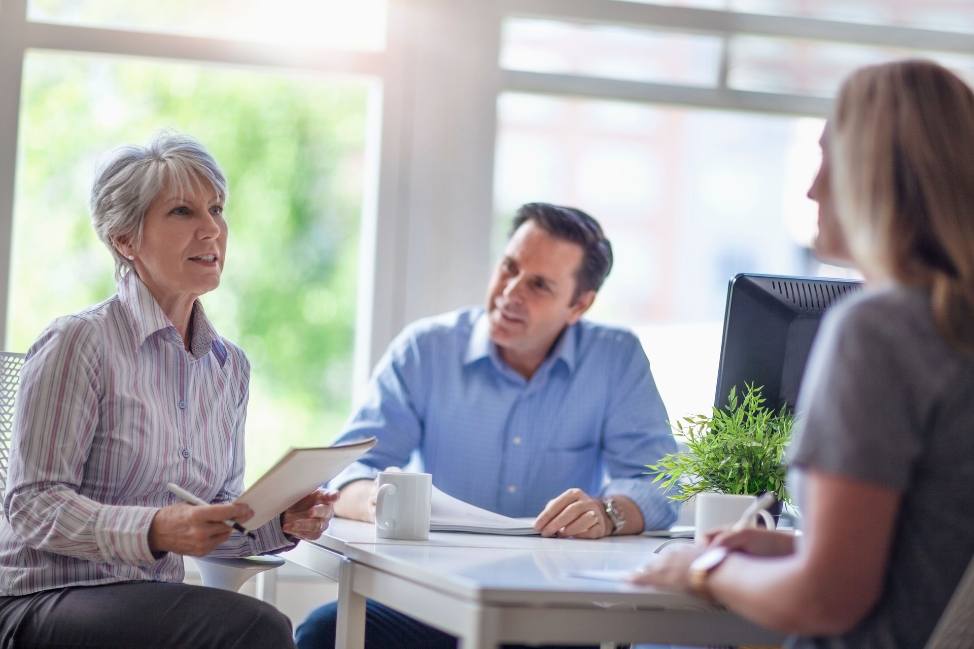 Senior Caucasian multiracial hispanic woman talks with colleagues in bright modern office